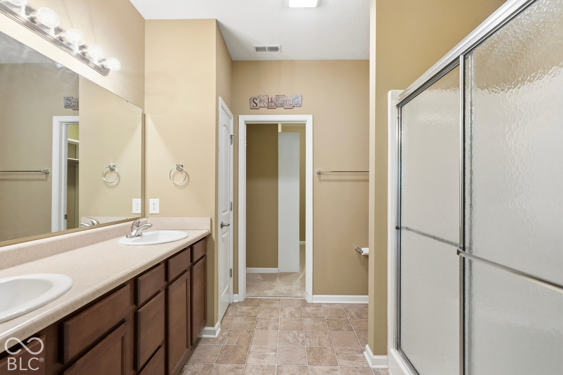 Double vanity with undermount sinks, expansive mirror, and a shower with sliding glass doors