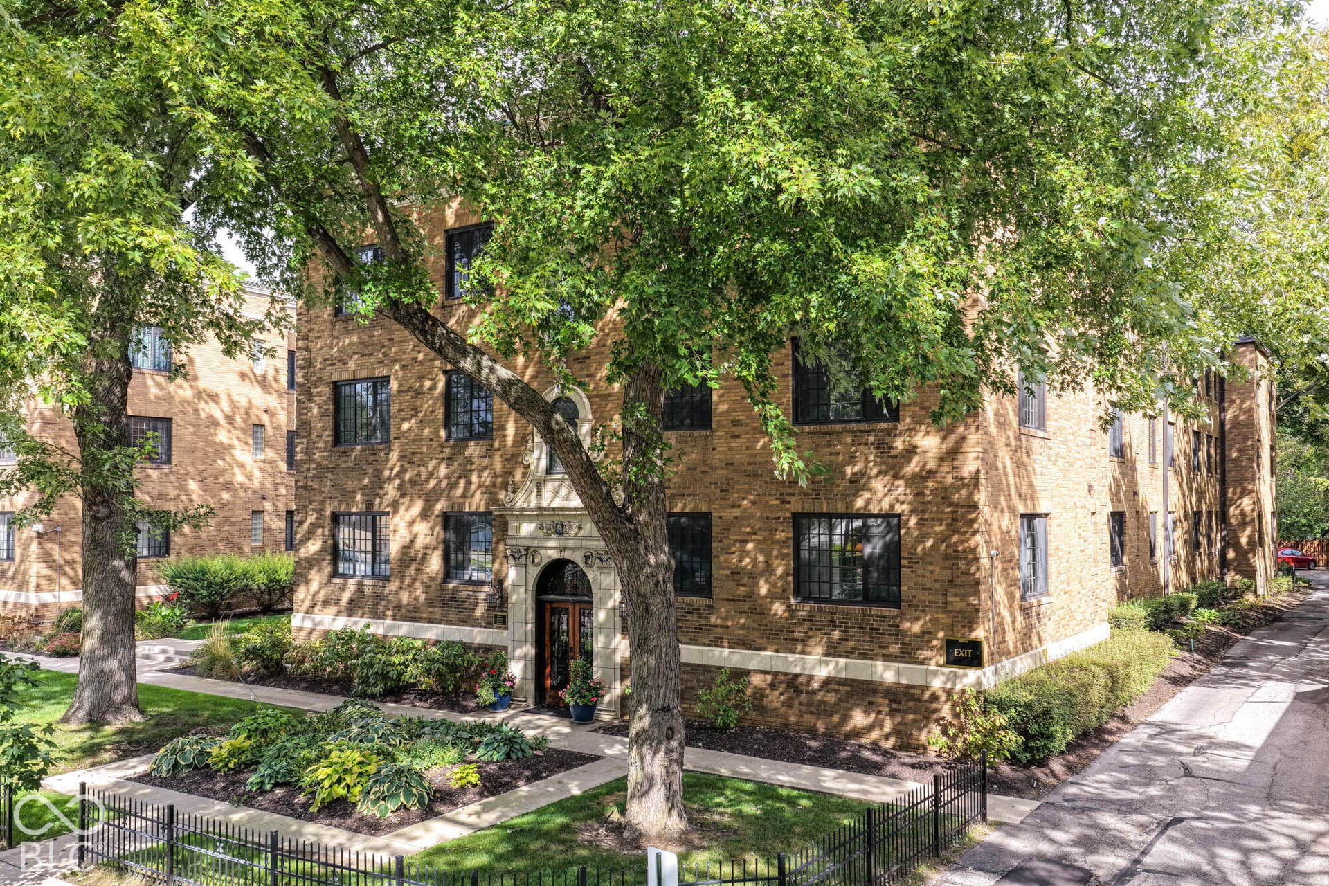 Brick exterior building featuring multiple windows with security bars, a stone-framed arched entry, and manicured landscaping
