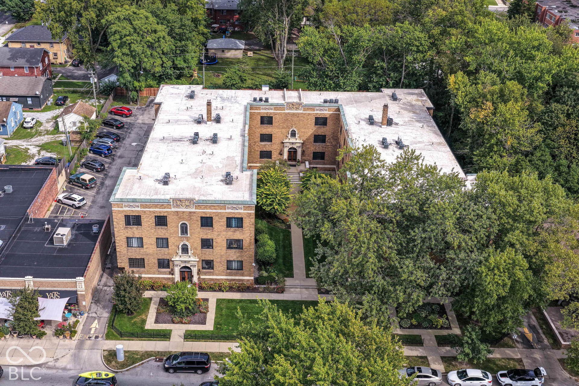 U-shaped building structure with brick facade, central courtyard, surface parking, and mature perimeter trees