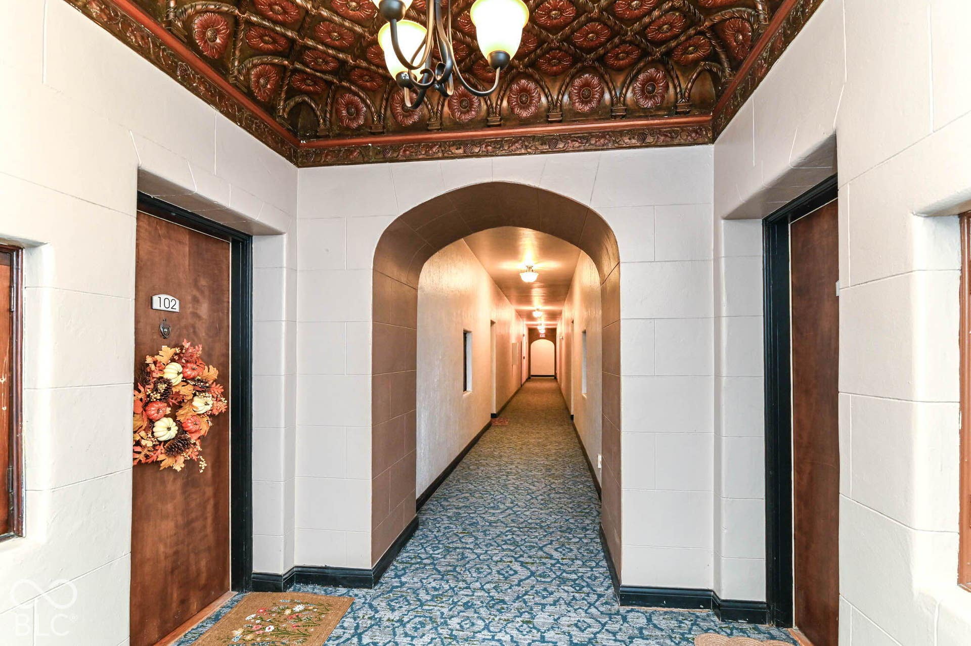 Ornate ceiling detailing, decorative chandelier, arched entryway, patterned carpeting, and panel doors