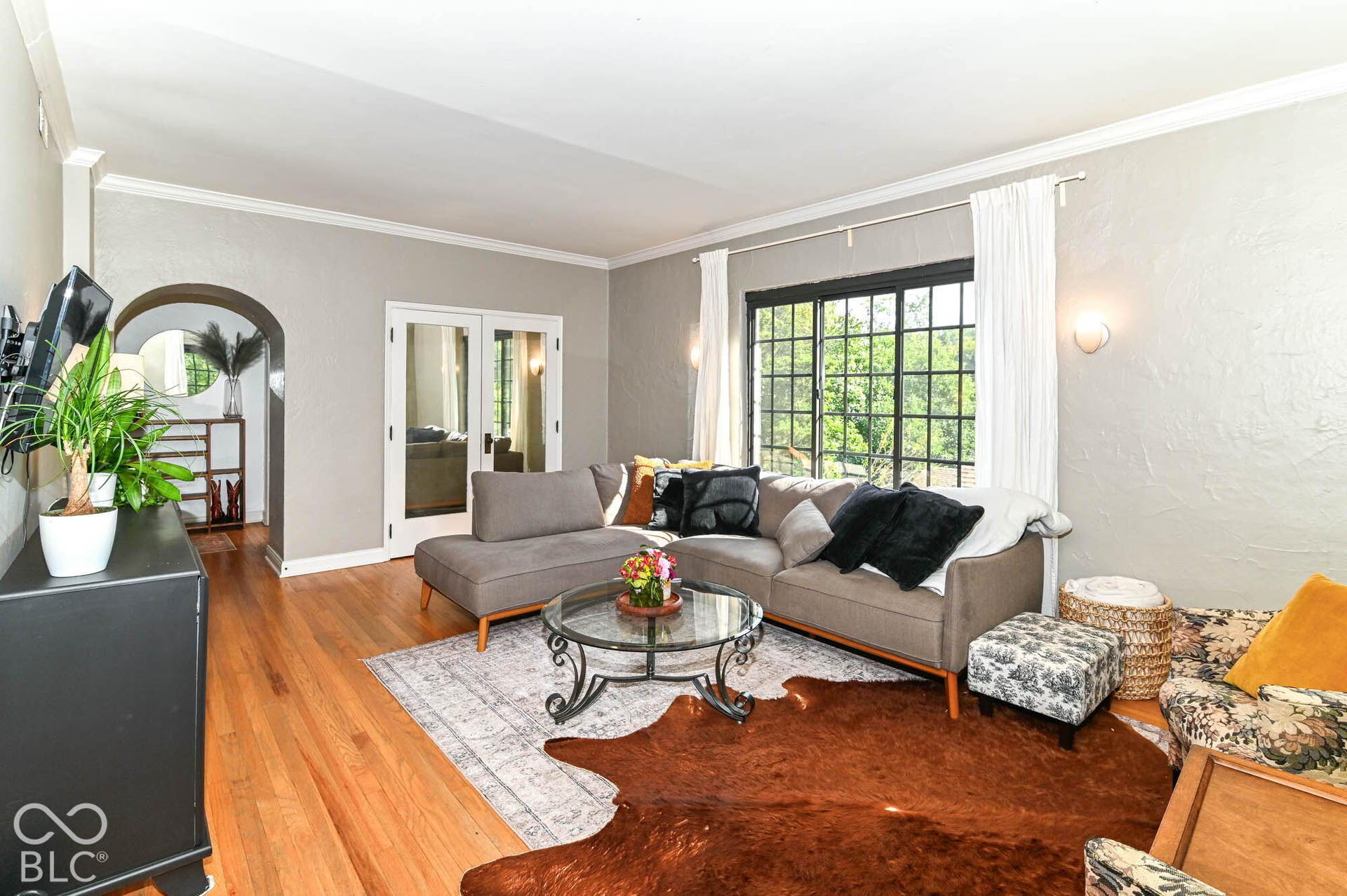Hardwood flooring, arched doorway, crown molding, French doors, and a large multi-pane window