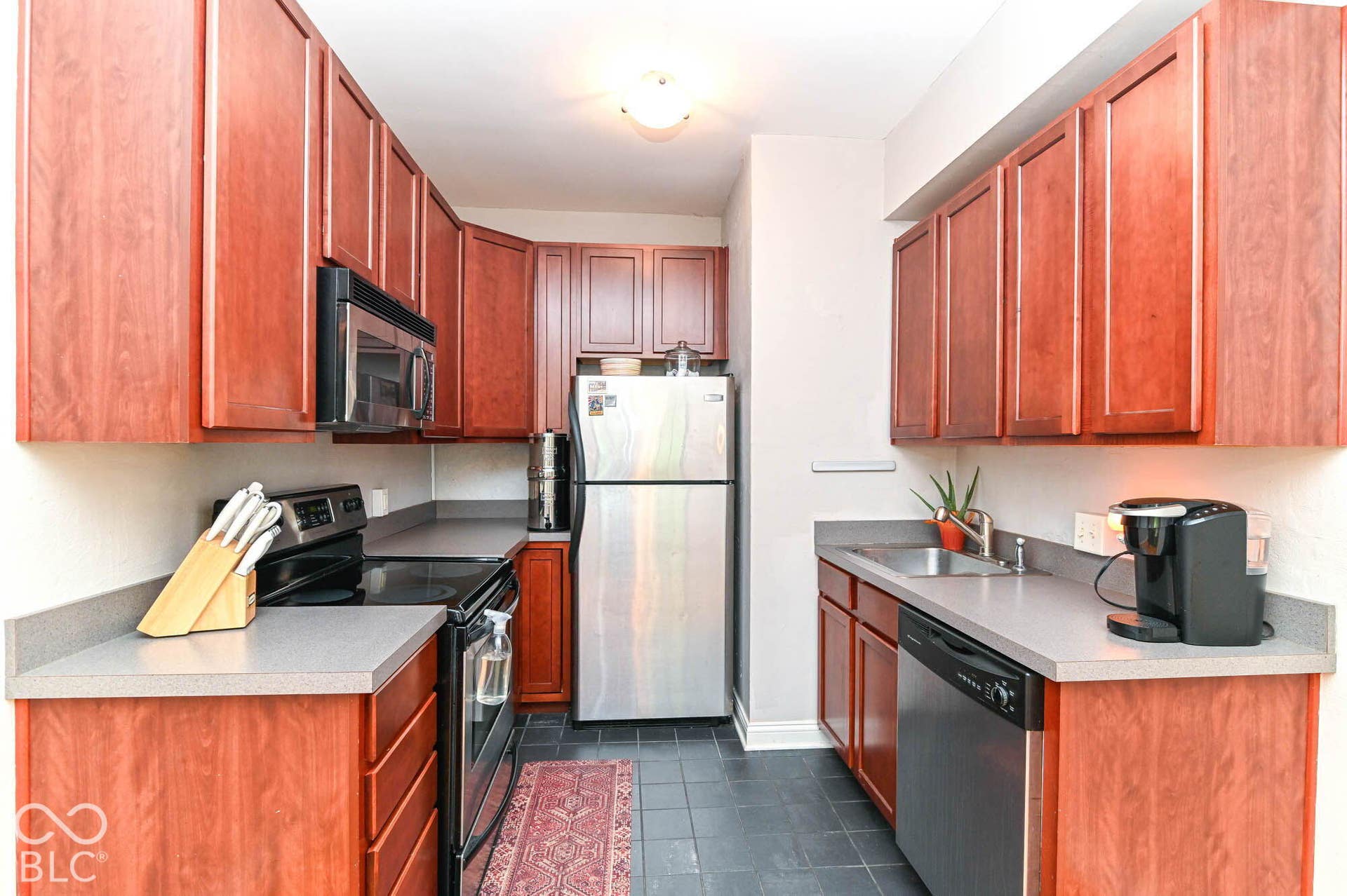 Kitchen featuring wood-finish cabinetry, stainless steel refrigerator, built-in microwave, black appliances, and dark tile flooring
