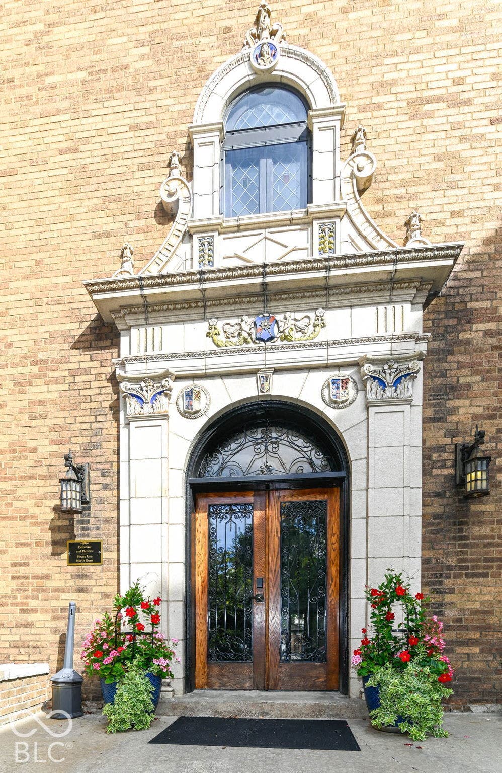 Ornate stone architectural facade with arched windows, double wood entry doors, and decorative wrought iron details