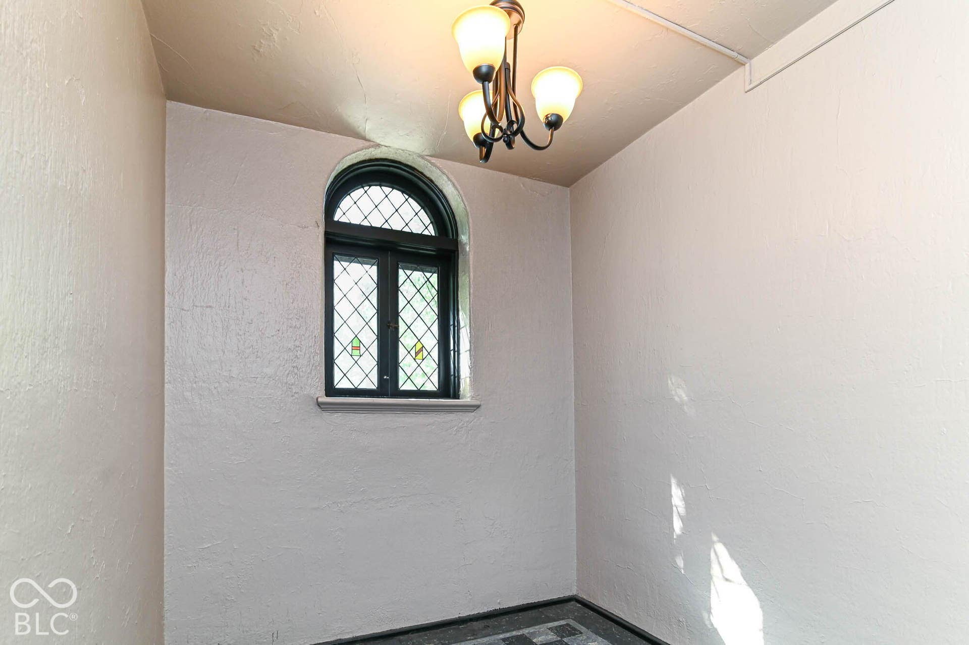 Arched window with leaded glass, mosaic tile flooring, and a multi-arm chandelier