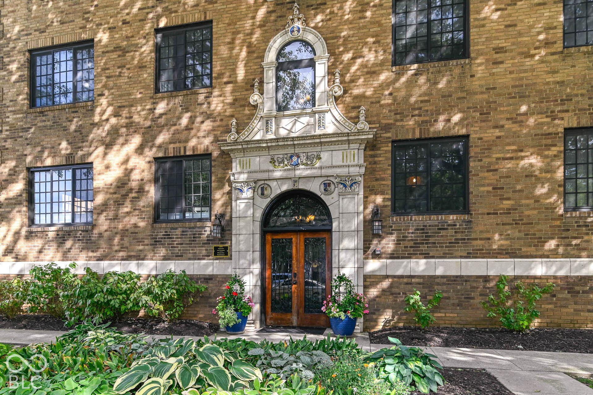 Brick facade with ornate stone entryway, arched double doors, and black-framed windows