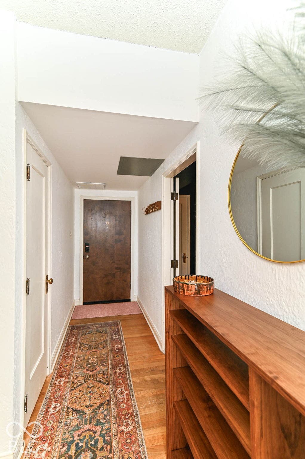 Hardwood flooring in a hallway with a solid wood entry door, multiple interior doors, and a built-in wood-finish shelving unit