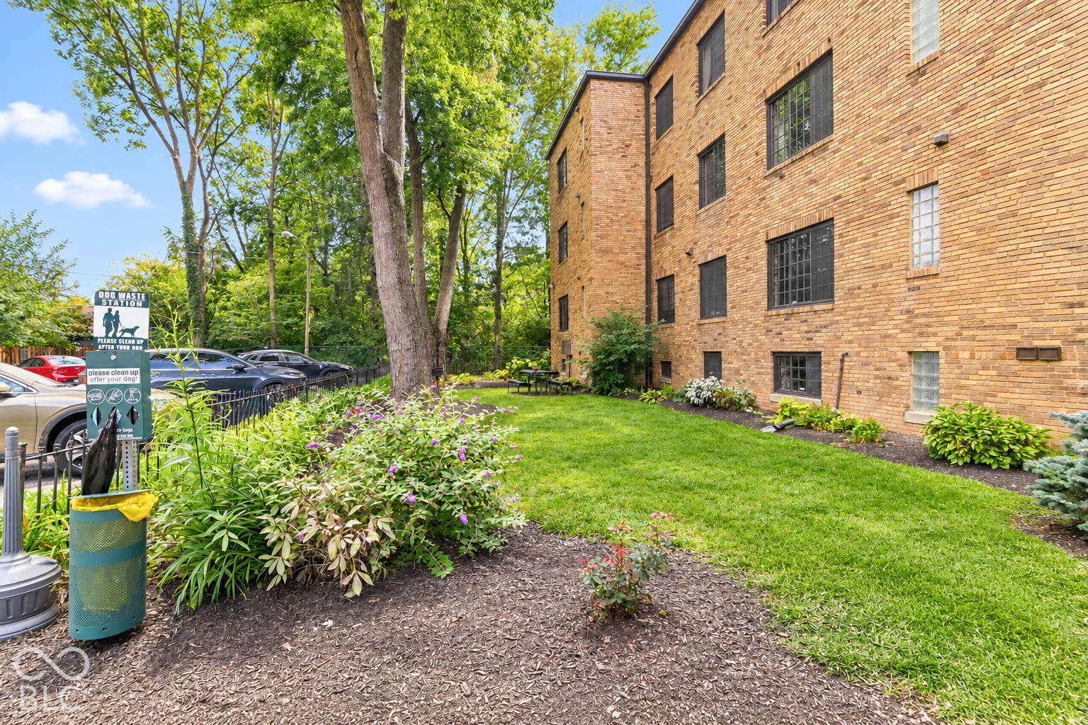 Brick exterior building with multiple windows, surrounded by green lawn, mature trees, and landscaping