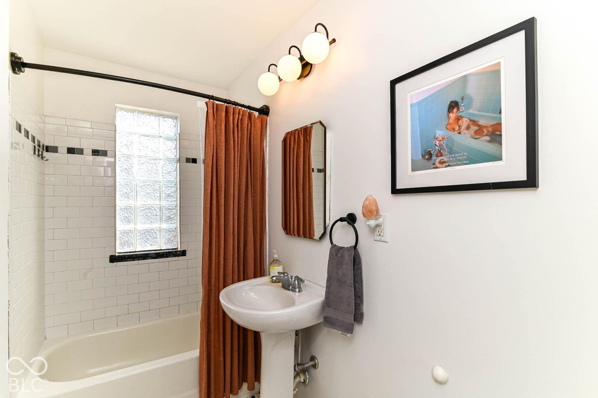 Bathtub with white subway tile surround, patterned accent tile, and glass block window