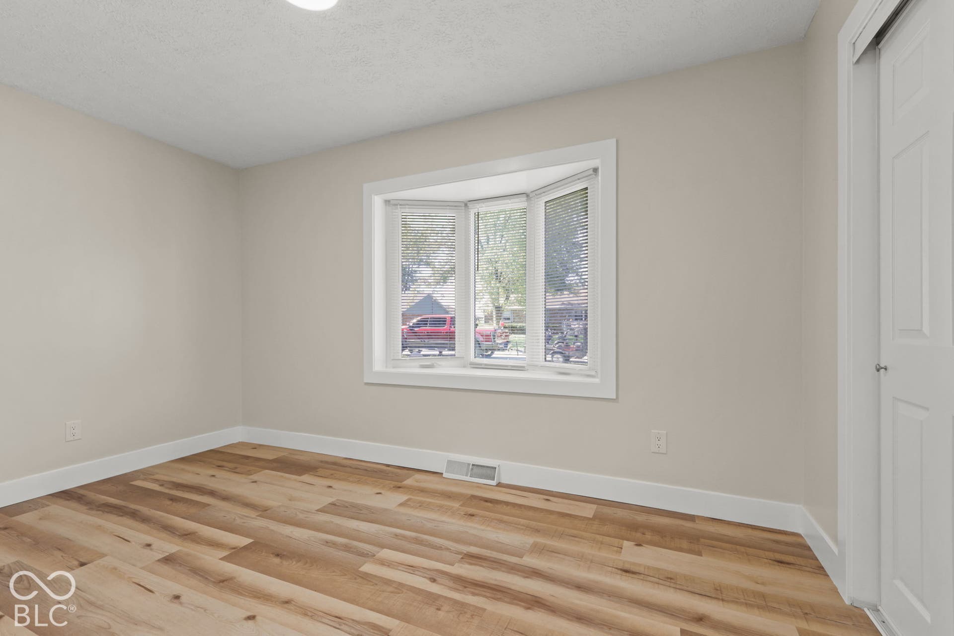 Bay window with white trim, wood-finish flooring, light-colored walls, white baseboards, and a white interior door