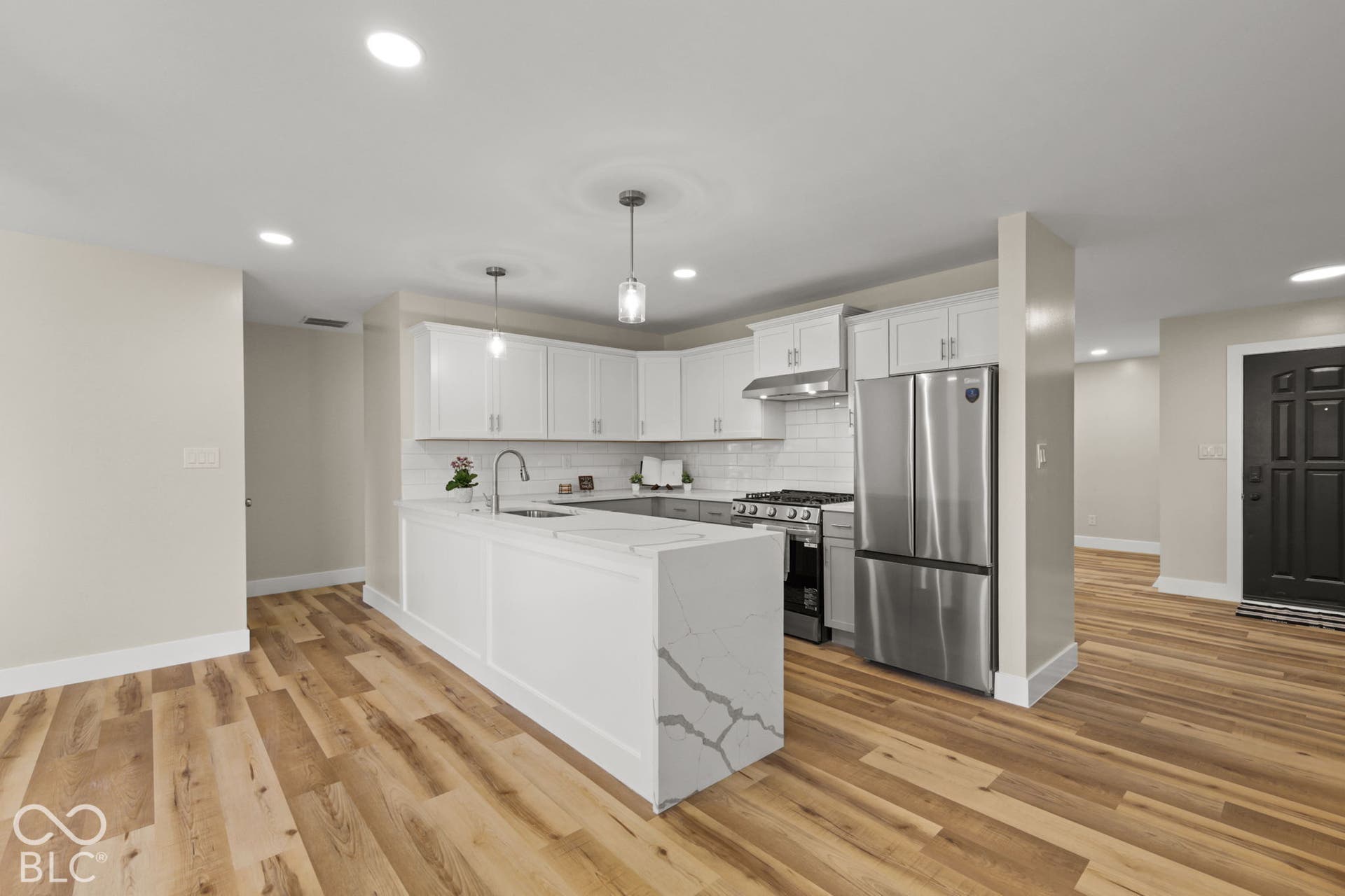 Kitchen featuring a central island with a waterfall countertop, stainless steel appliances, white shaker cabinetry, and wood-finish flooring
