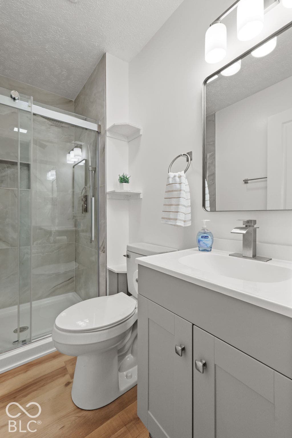 Modern bathroom featuring a glass-enclosed shower with tile surround, white toilet, single vanity with a white countertop, and wood-finish flooring