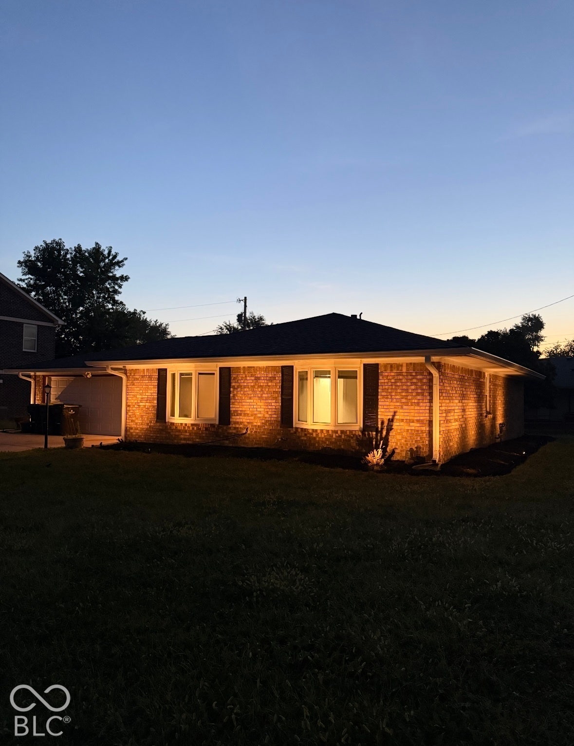 Brick exterior with a dark shingle roof, featuring multiple bay windows, and a covered carport