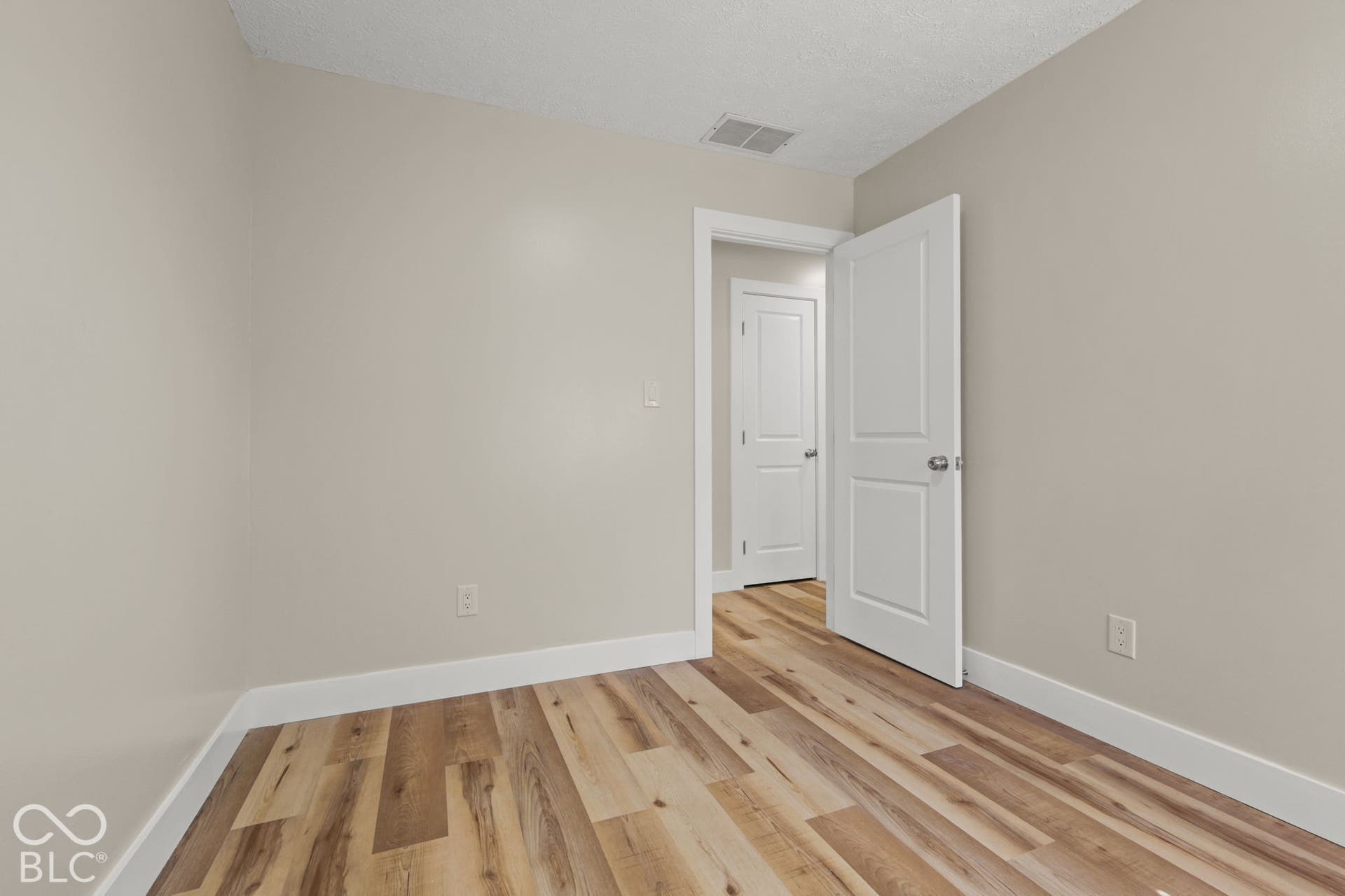 Wood-finish flooring with light neutral wall tones, white trim, and a white interior door