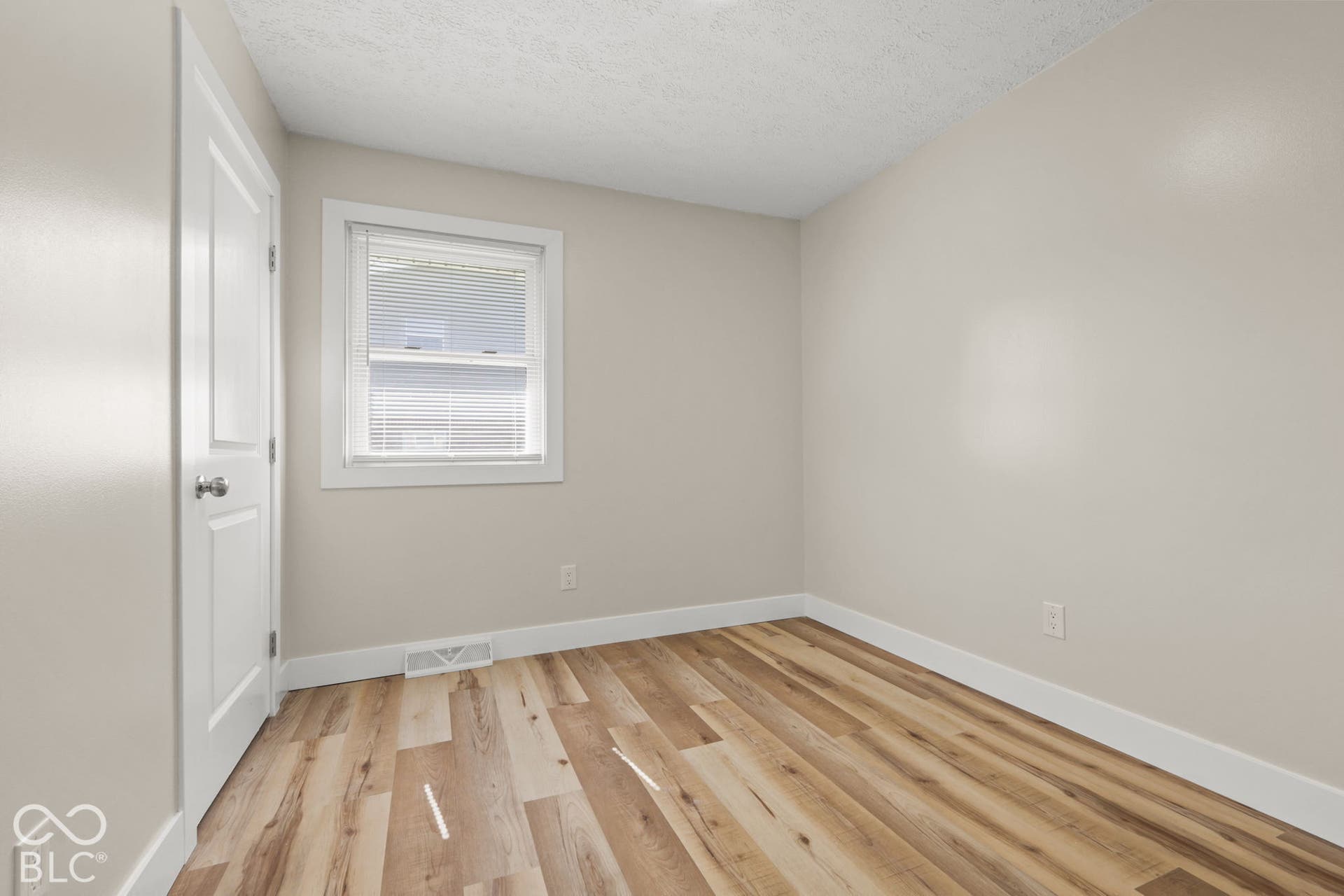 Wood-finish flooring with white trim, a single window with blinds, and light-toned wall finishes