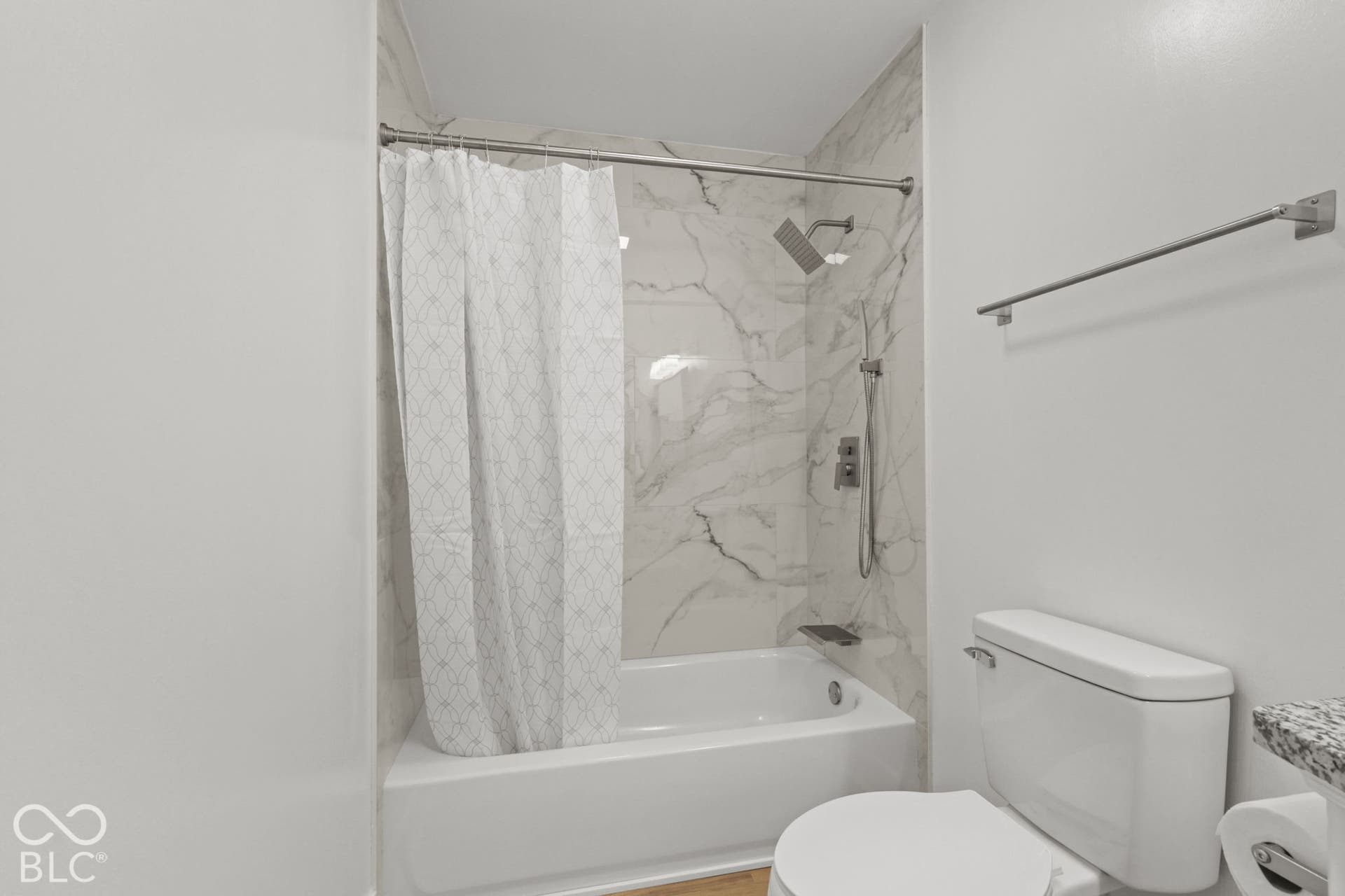 Bathtub and shower combination featuring marble-finish tile surround and a rain shower head