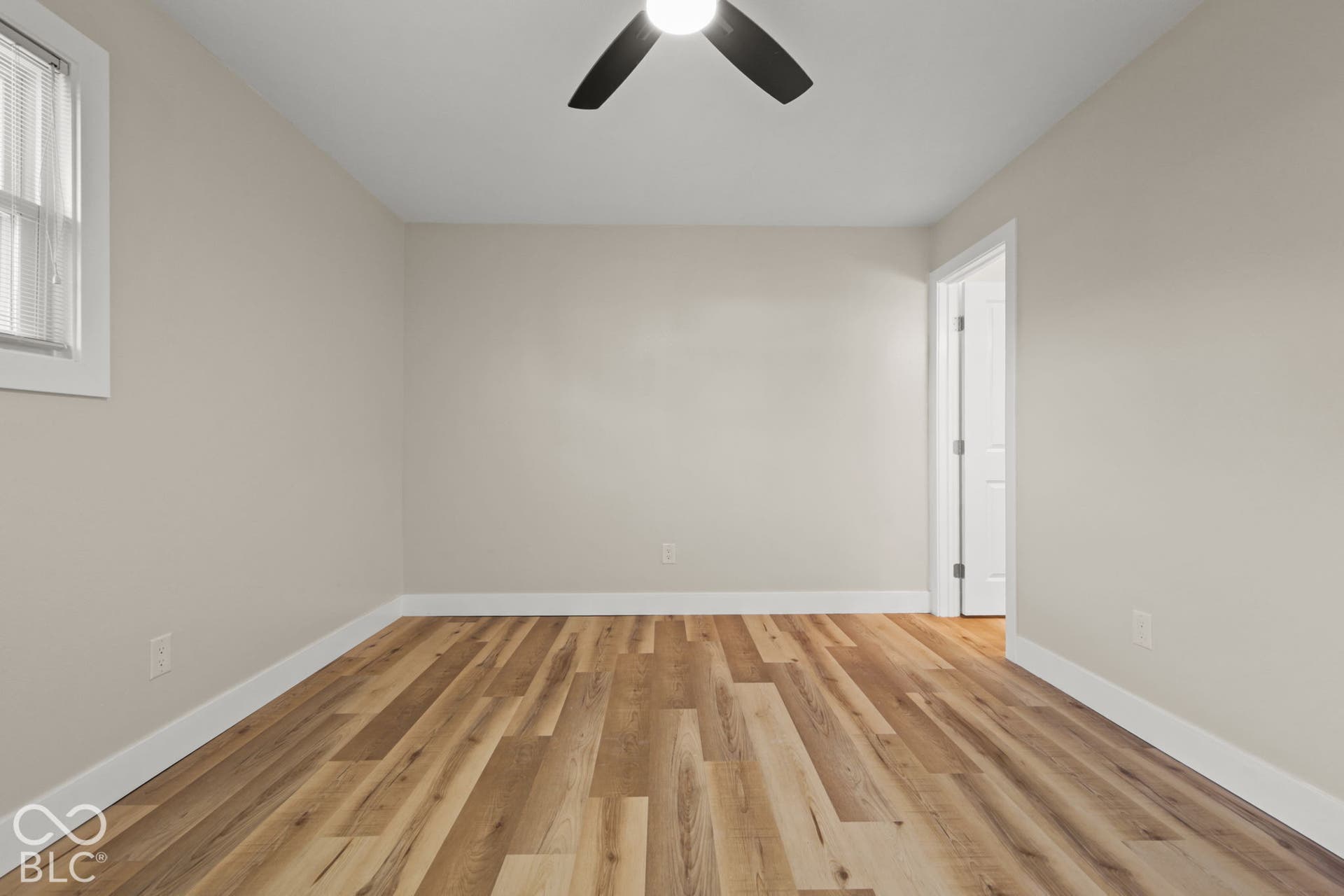 Wood-finish flooring, light neutral wall paint, white trim, window with blinds, and a ceiling fan