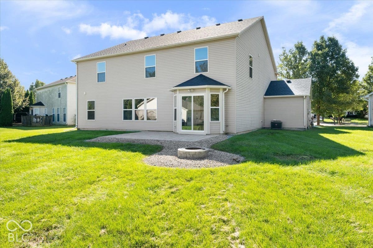 11780 Copper Mines Way, Fishers, IN 46038 Expansive rear yard featuring a concrete patio, a stone-lined fire pit area, and a bay window extension with sliding glass doors