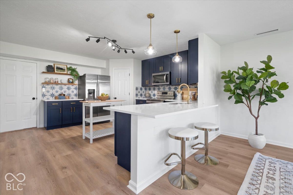 11780 Copper Mines Way, Fishers, IN 46038 Wood-finish flooring, white walls, navy cabinetry with gold-toned hardware, patterned backsplash, and an island with a white countertop