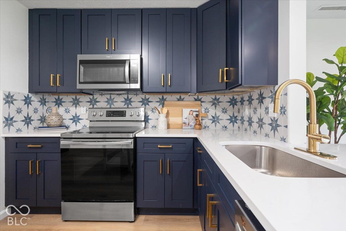 11780 Copper Mines Way, Fishers, IN 46038 Navy blue cabinetry with brass hardware, patterned tile backsplash, stainless steel appliances, white countertops, and wood-finish flooring