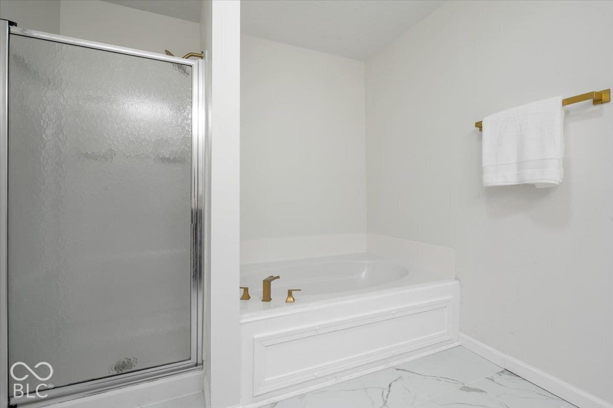 11780 Copper Mines Way, Fishers, IN 46038 Frosted glass shower enclosure, corner soaking tub with gold-tone fixtures, white paneling on tub surround, and light-toned patterned floor tile