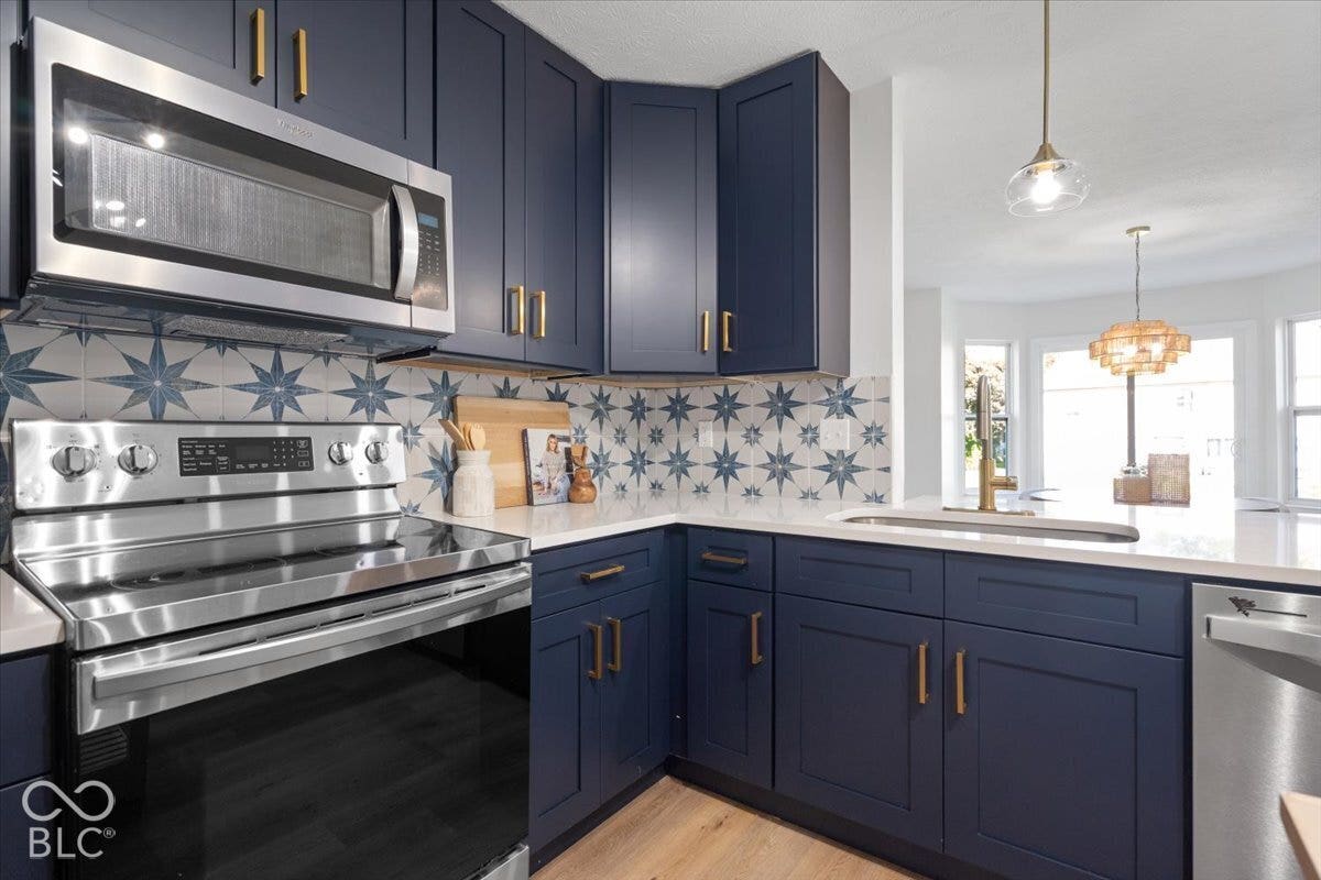 11780 Copper Mines Way, Fishers, IN 46038 Navy cabinetry with brass hardware, patterned tile backsplash, stainless steel appliances, white countertops, and wood-finish flooring