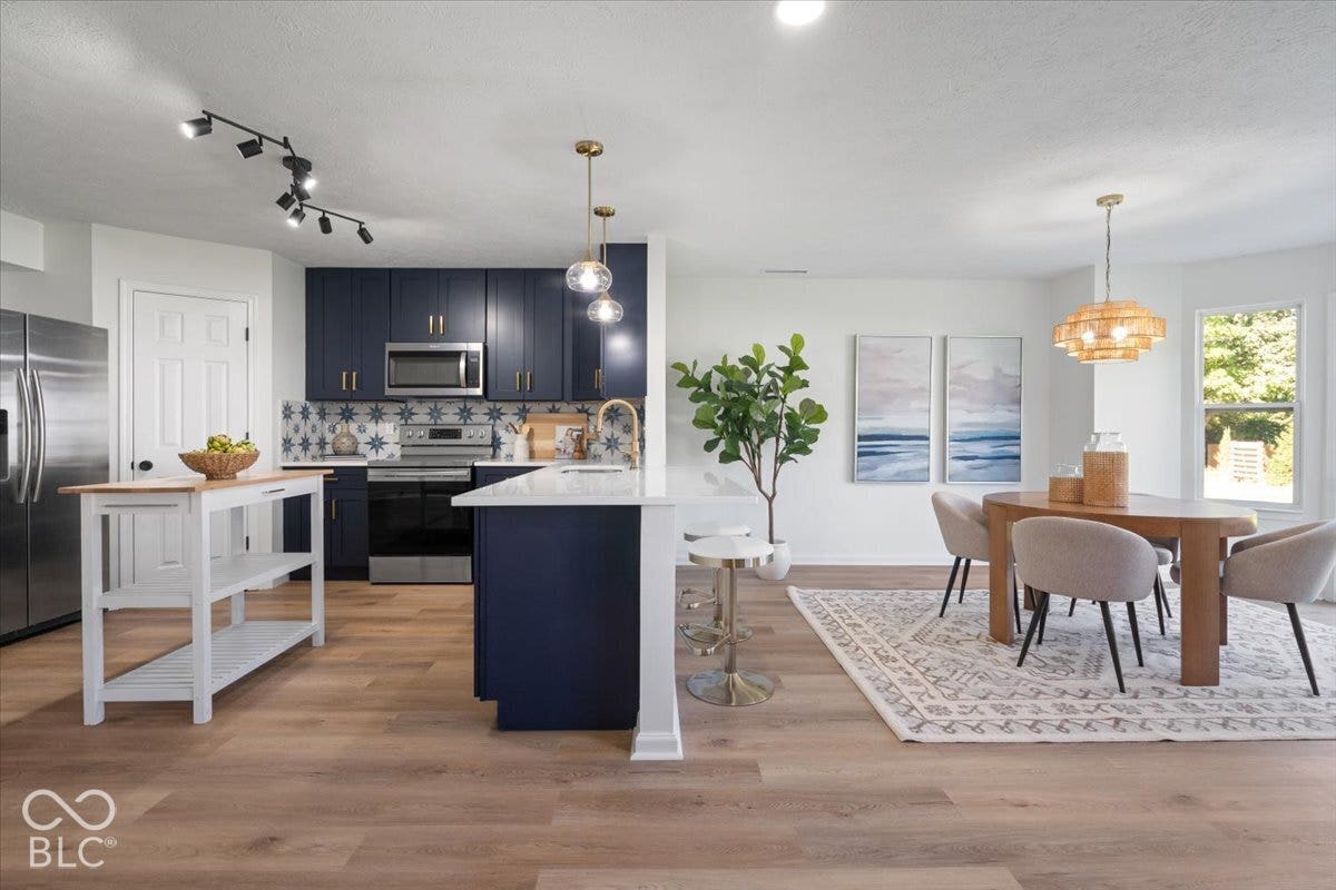 11780 Copper Mines Way, Fishers, IN 46038 Kitchen and dining area featuring wood-finish flooring, dark blue cabinetry, stainless steel appliances, and a kitchen island with seating