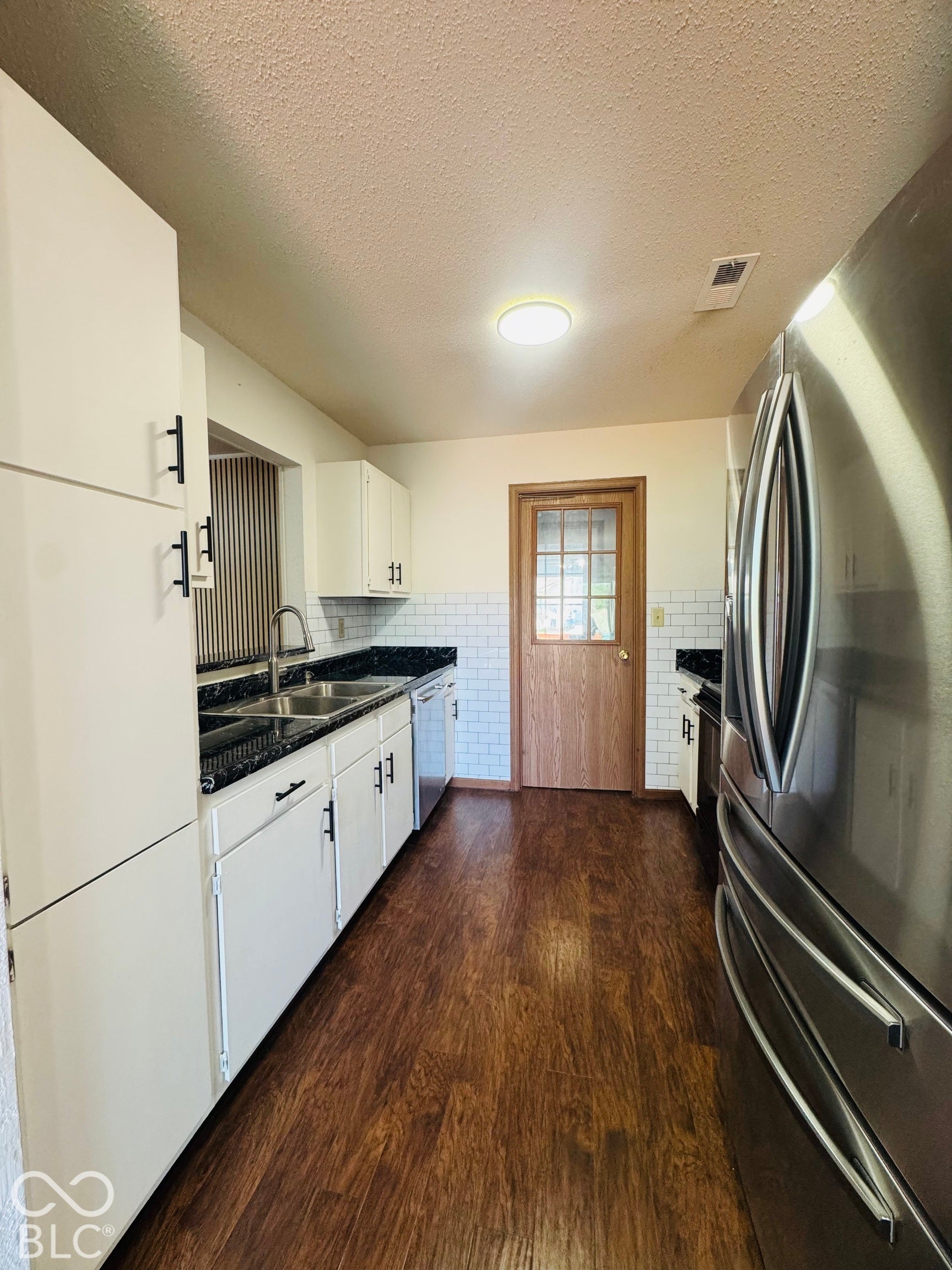 Kitchen with white cabinetry, dark countertops, wood-finish flooring, and white subway tile backsplash