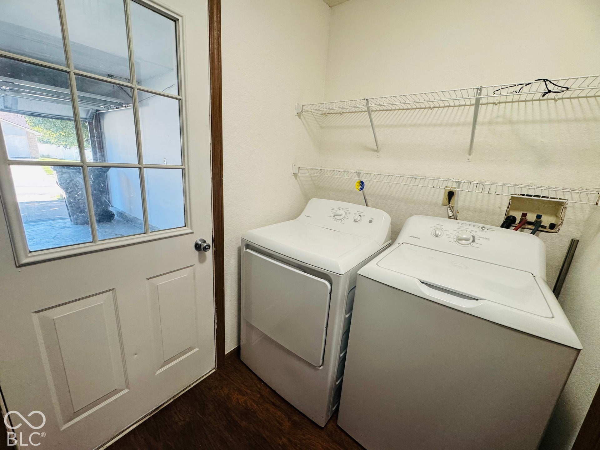 Laundry area featuring wood-finish flooring, two white appliances, and a white paneled door with glass inserts