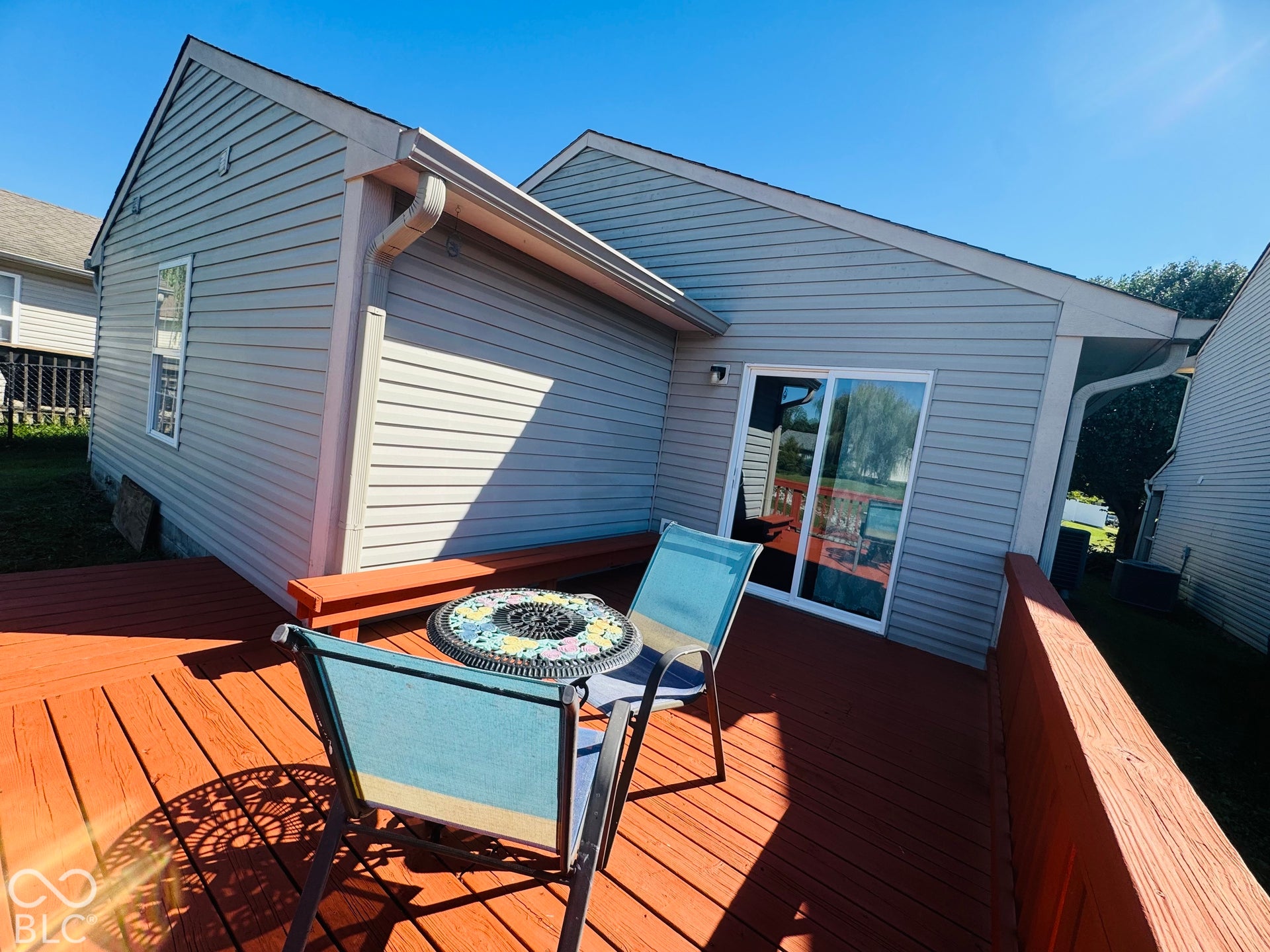 Wood-finish deck with a built-in bench, gray siding, and white sliding glass door