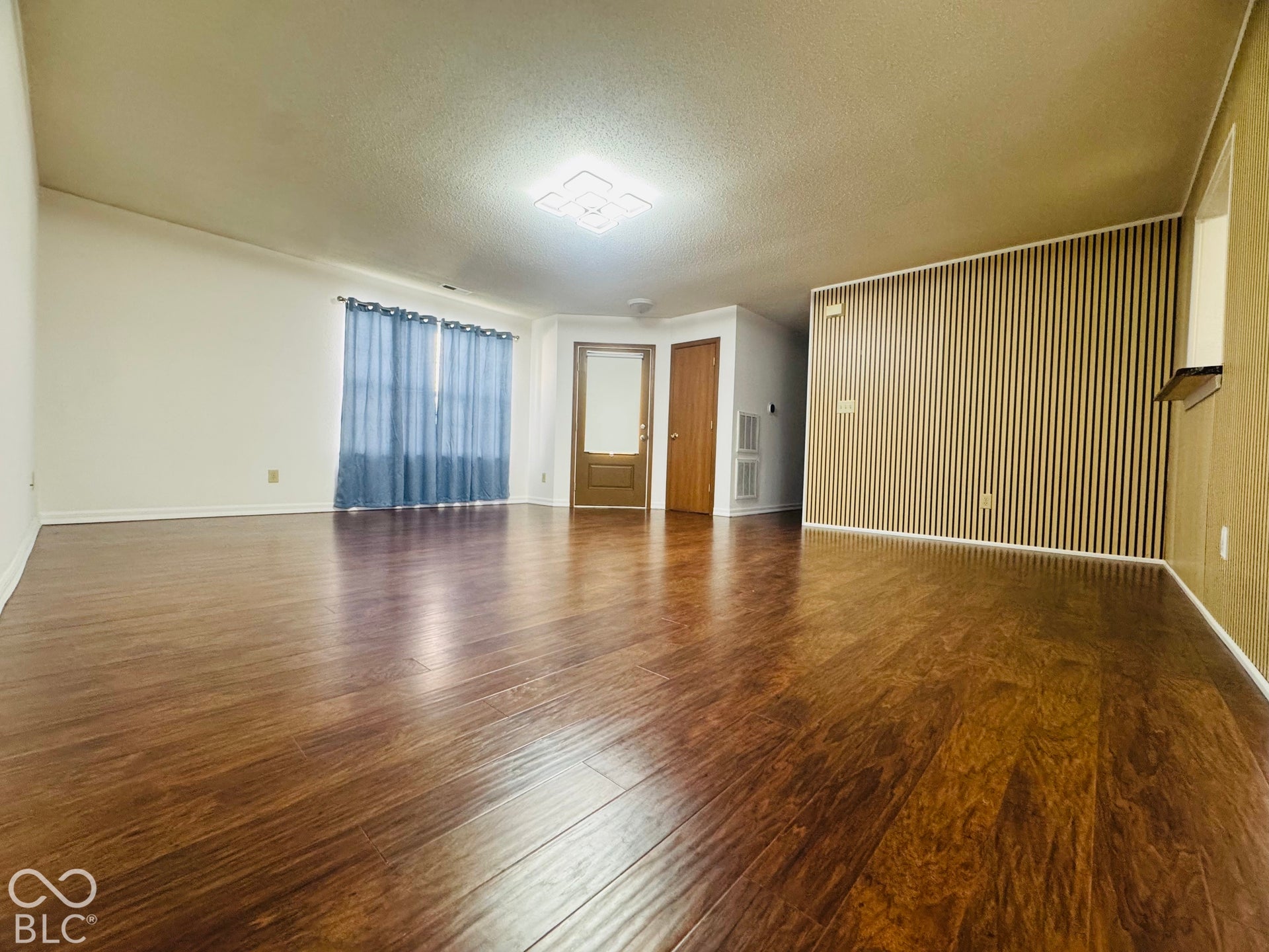 Expansive open living area featuring wood-finish flooring, a contemporary ceiling light fixture, and a decorative slatted accent wall