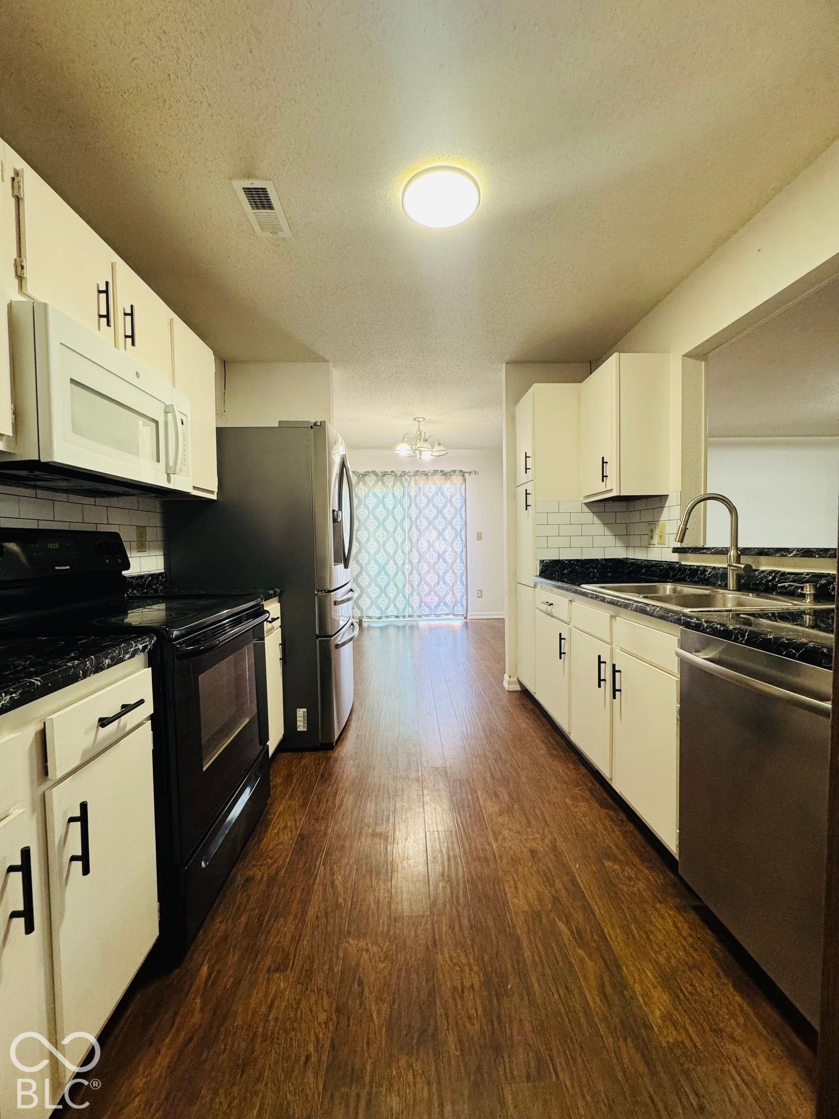 Kitchen featuring wood-finish flooring, white cabinetry, black countertops, stainless steel appliances, and subway tile backsplash