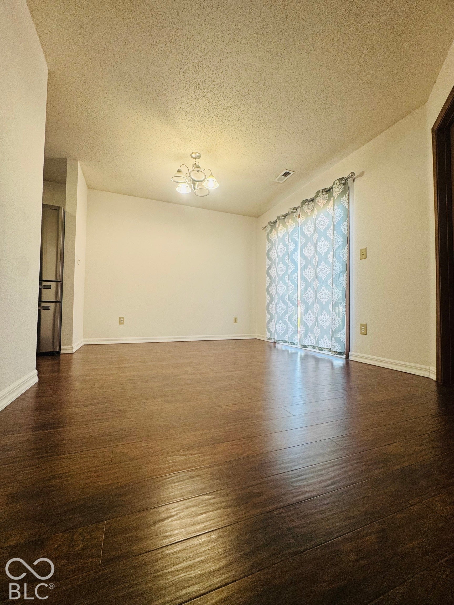 Spacious room featuring rich wood-finish flooring, a contemporary ceiling light fixture, and a sliding glass door