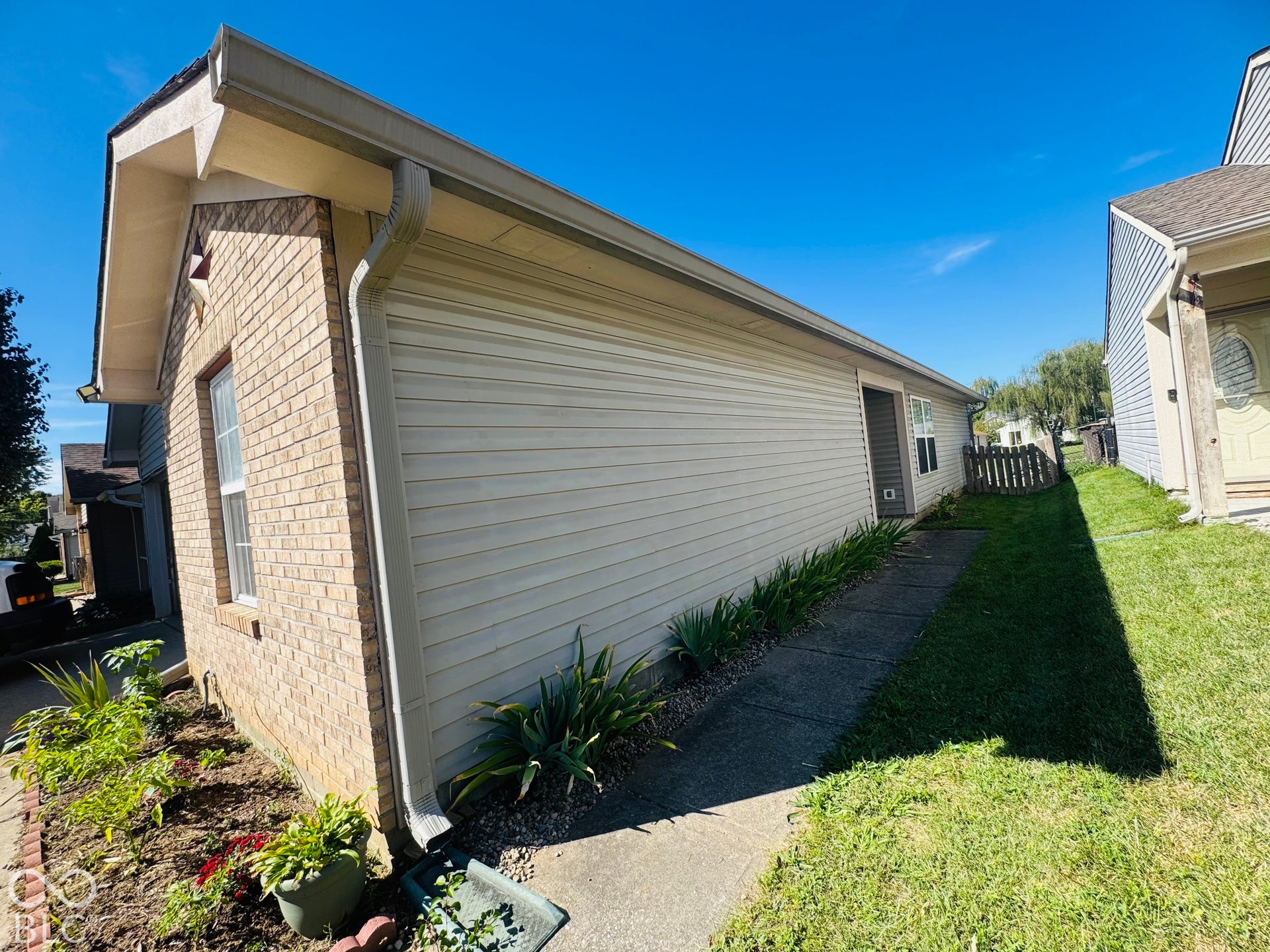 Brick and siding exterior with a concrete walkway, landscaped border, and a wood fence in the distance