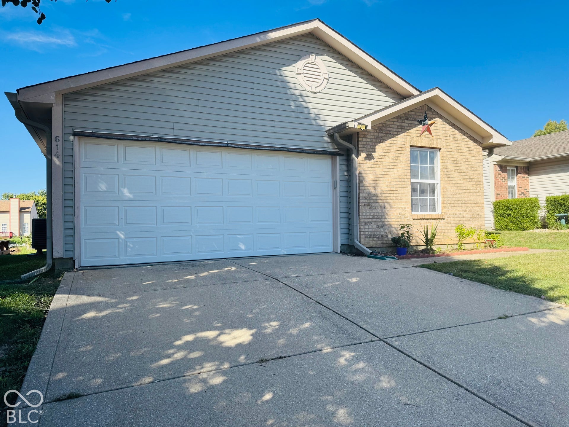 Brick and siding exterior with an attached garage, concrete driveway, and established landscaping
