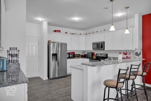 White cabinetry, stainless steel appliances, breakfast bar, pendant lighting, and wood-finish flooring