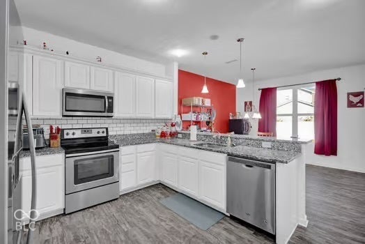 Kitchen featuring granite countertops, white cabinetry, stainless steel appliances, a tile backsplash, and wood-finish flooring