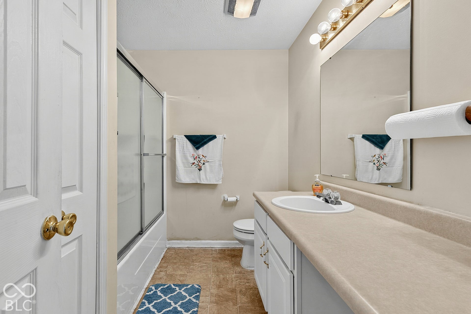 Sliding glass shower enclosure, single vanity with integrated sink, expansive countertop, white cabinetry, and wall-mounted mirror