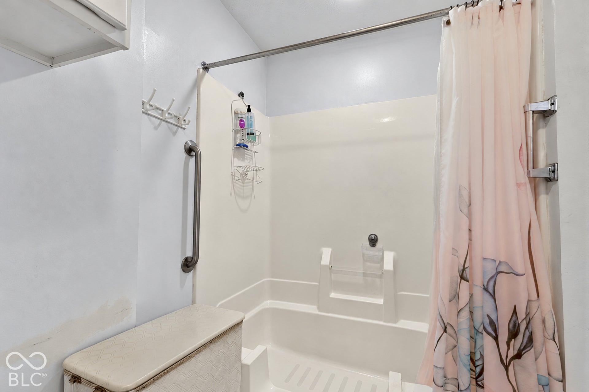 White shower-over-tub unit with a grab bar and a built-in shelf