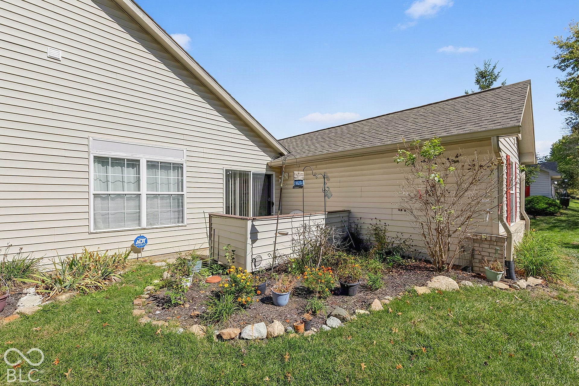 Side exterior with vinyl siding, shingle roofing, a sliding glass door, and a built-in garden bed