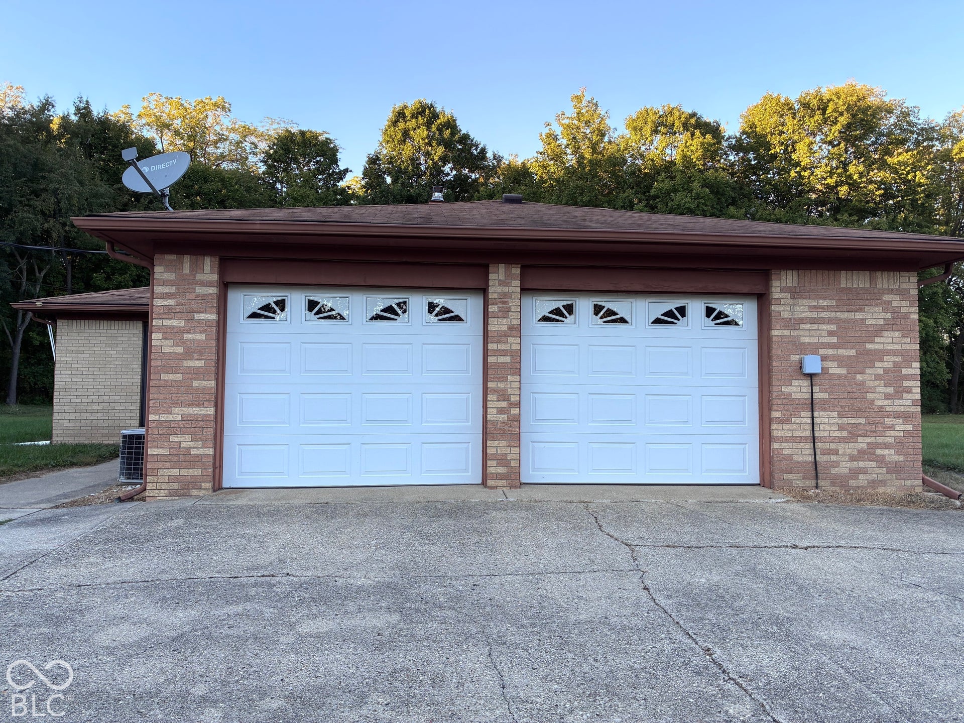 Attached two-car garage with brick veneer siding, brown trim, and white paneled garage doors featuring decorative window inserts
