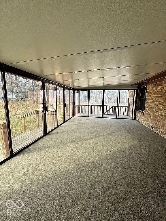 Enclosed sunroom featuring full-height glass panels, neutral carpeting, a light-colored ceiling, and direct access to an outdoor deck