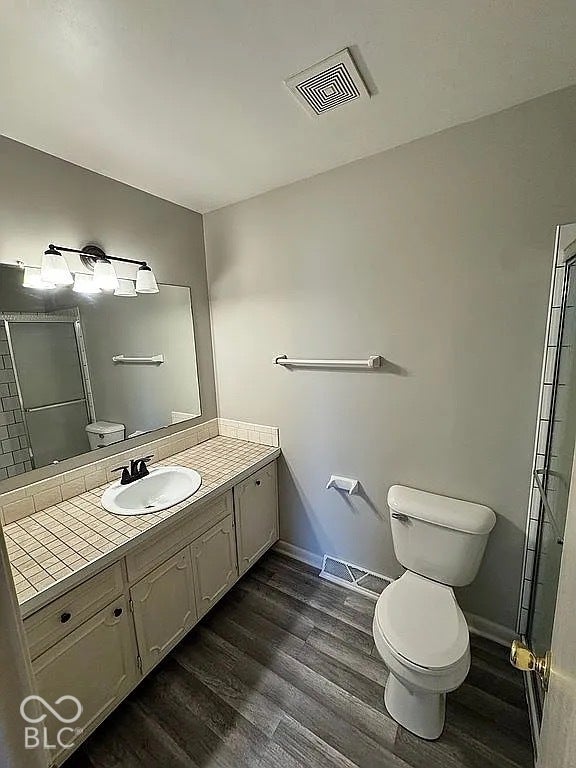 Vanity with an integrated sink, tile countertop, wood-finish flooring, and a shower enclosure with subway tile