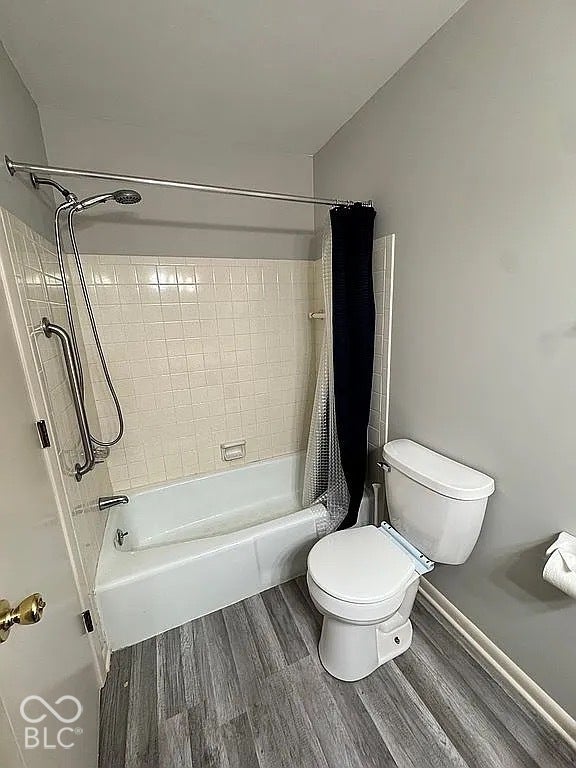 Tub/shower combination with white tile surround, a white toilet, and wood-finish flooring