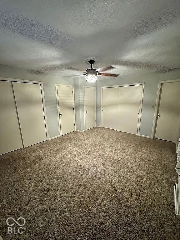 Carpeted room featuring a ceiling fan with light fixture, multiple doors, and light-colored walls