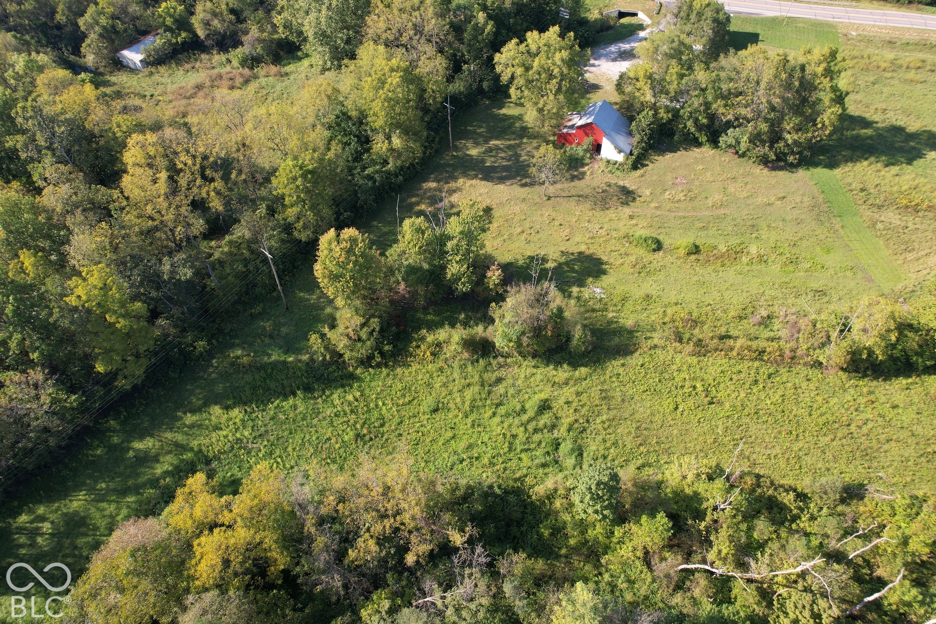 Expansive green acreage with a red and white outbuilding and surrounding mature trees