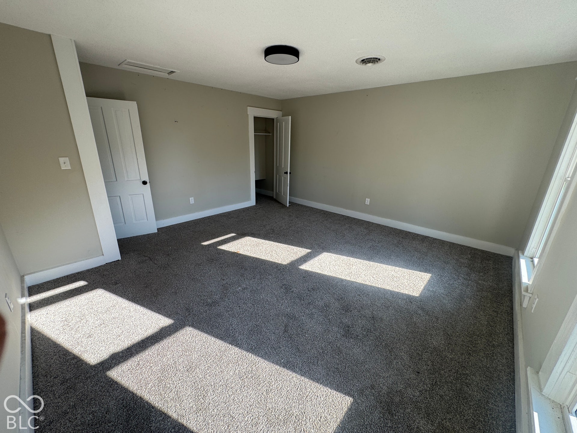 Plush gray carpeting, neutral wall color, and a modern flush-mount ceiling light