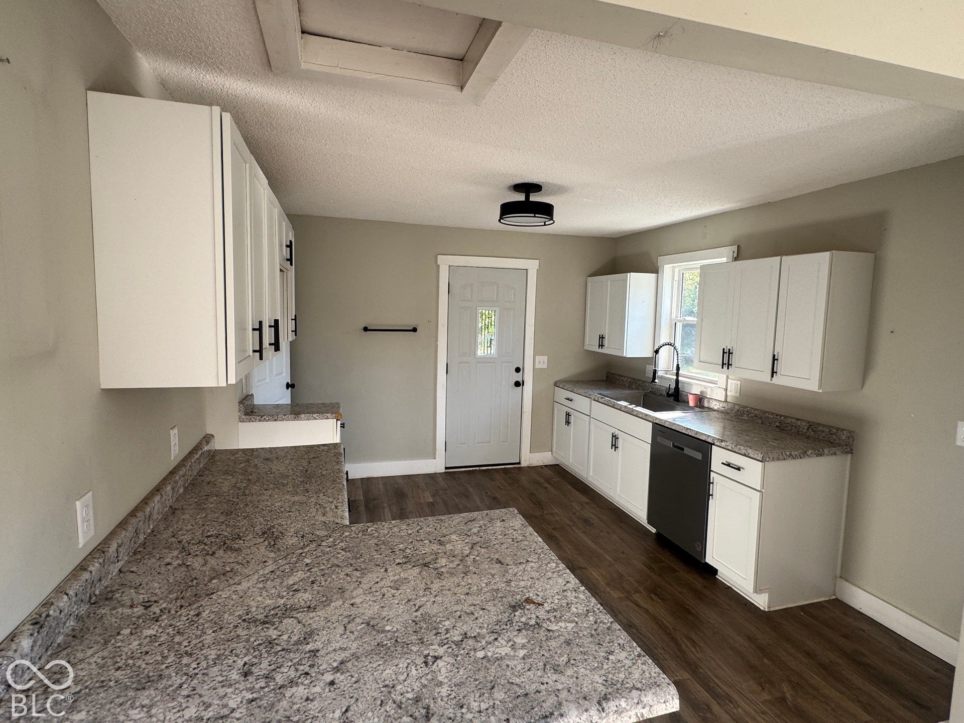 L-shaped countertop with integrated sink, white cabinetry with black hardware, wood-finish flooring, and recessed lighting