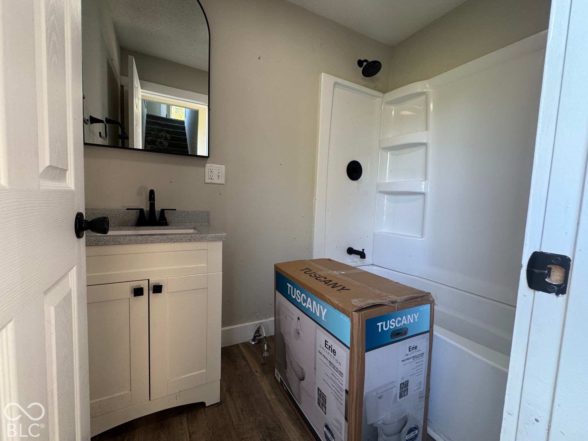 White vanity with gray speckled countertop, black faucet, and arched mirror
