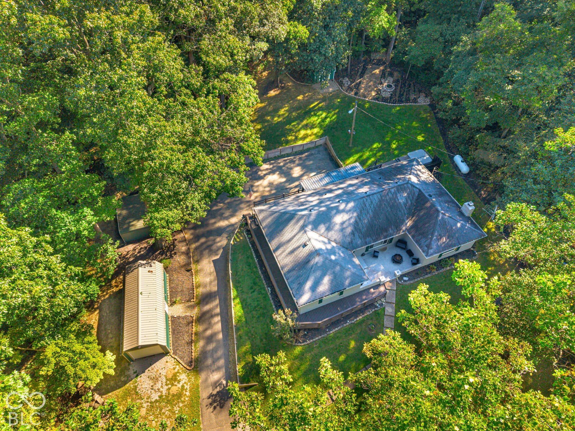 Expansive property with a dwelling and detached storage structure, surrounded by mature trees