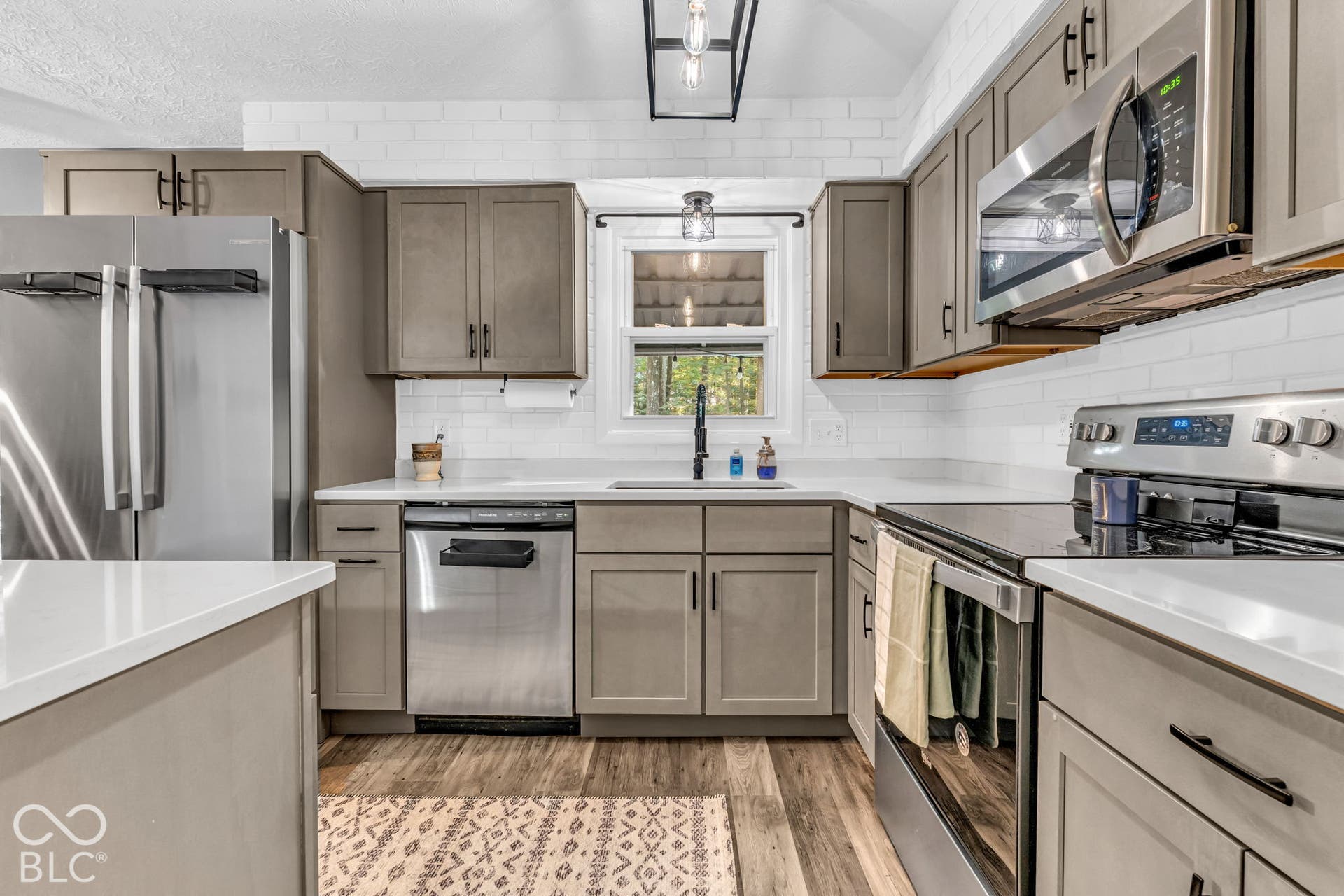Stainless steel appliances, white subway tile backsplash, white countertops, wood-finish flooring, and shaker-style cabinetry